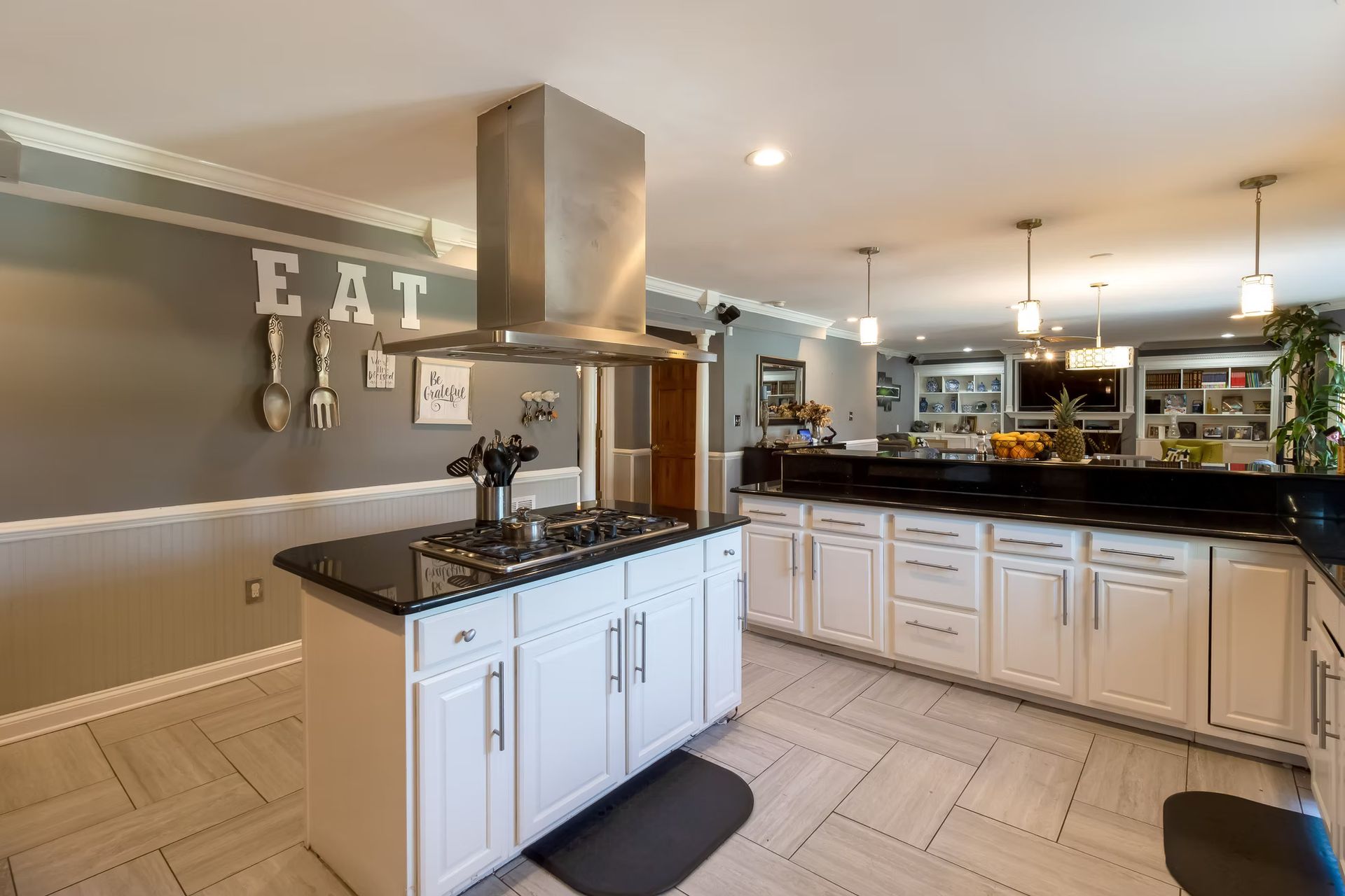 Modern kitchen with white cabinets, black countertops, and a stainless-steel range hood and island