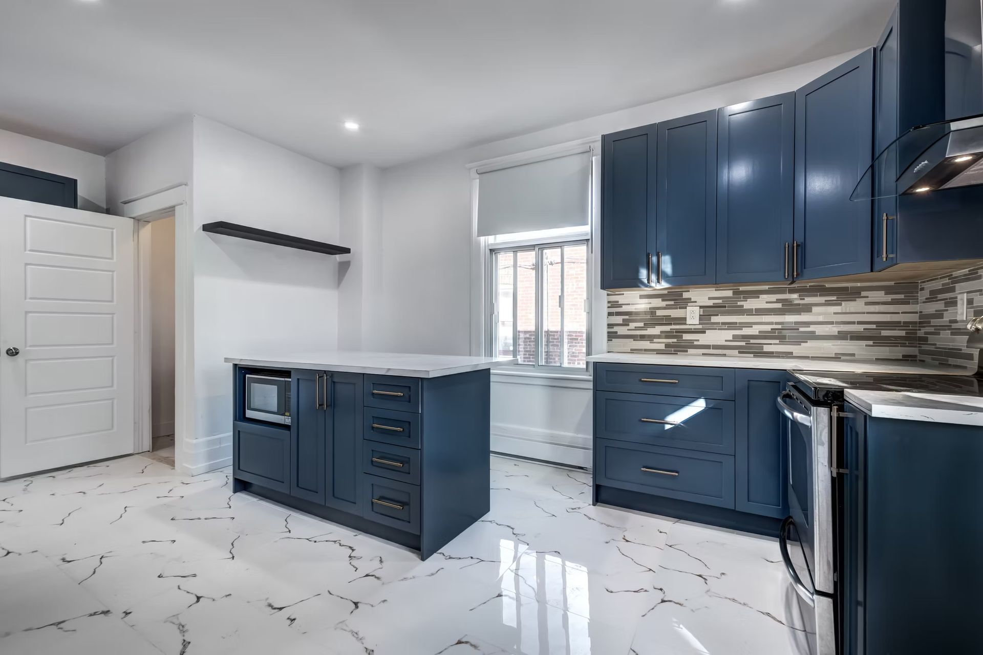 Modern kitchen with navy cabinets, white marble floor, stainless appliances, and window above the sink