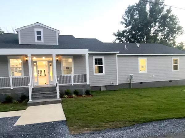 Gray house with a lit front porch, white trim, and a front lawn at dusk