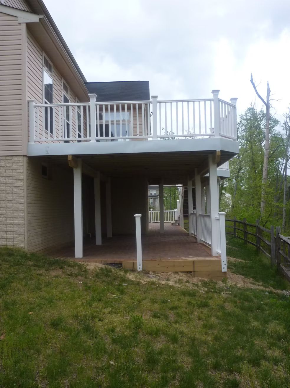 Raised deck with white railing and stairs above a grassy backyard, supported by posts underneath