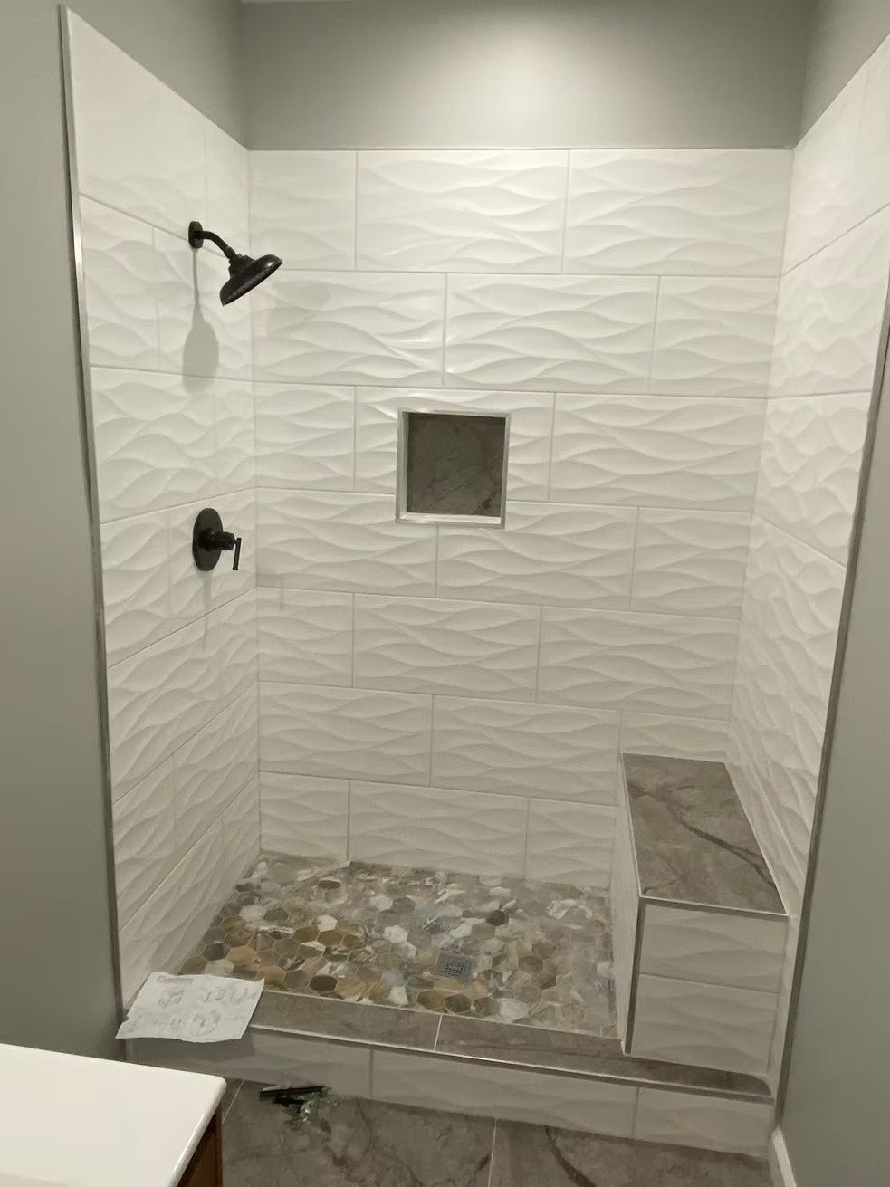 Small tiled walk-in shower with pebble floor, wall niche, and bench seat