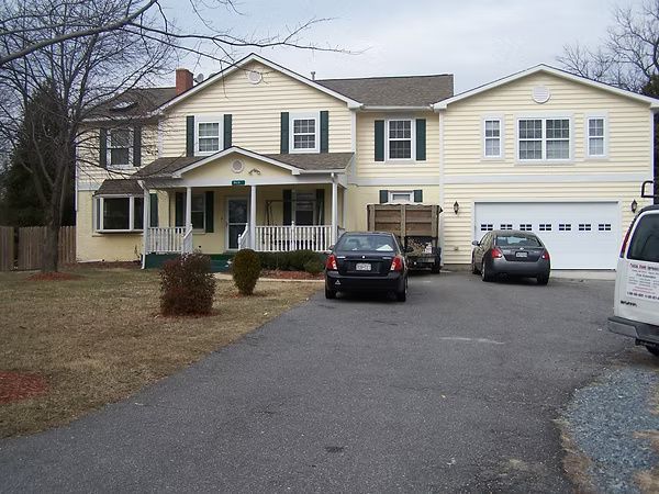 Suburban two-story yellow house with driveway, parked cars, and attached garage