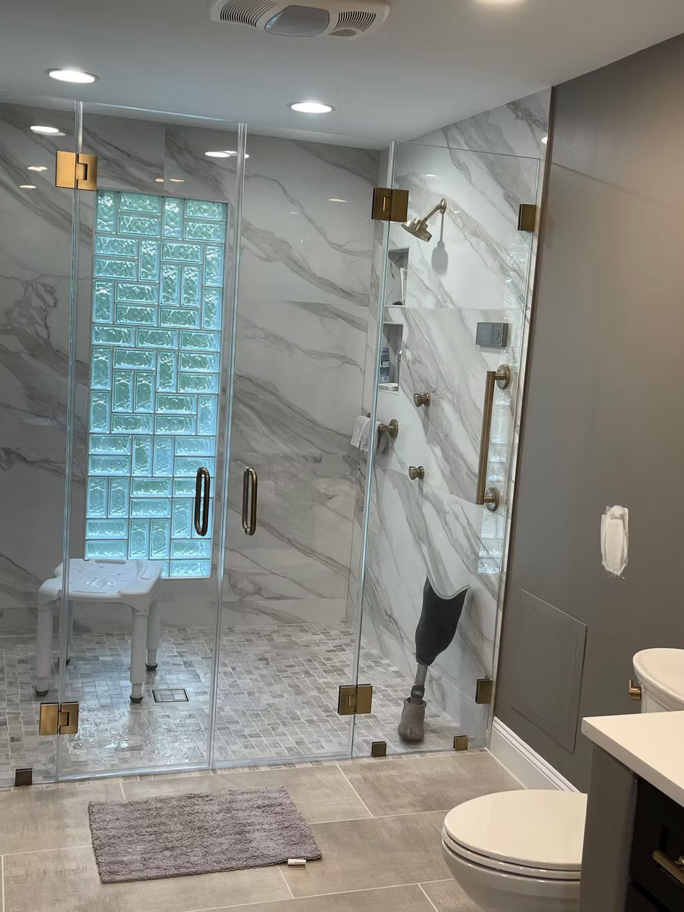 Modern bathroom with glass walk-in shower, marble walls, and toilet beside a vanity