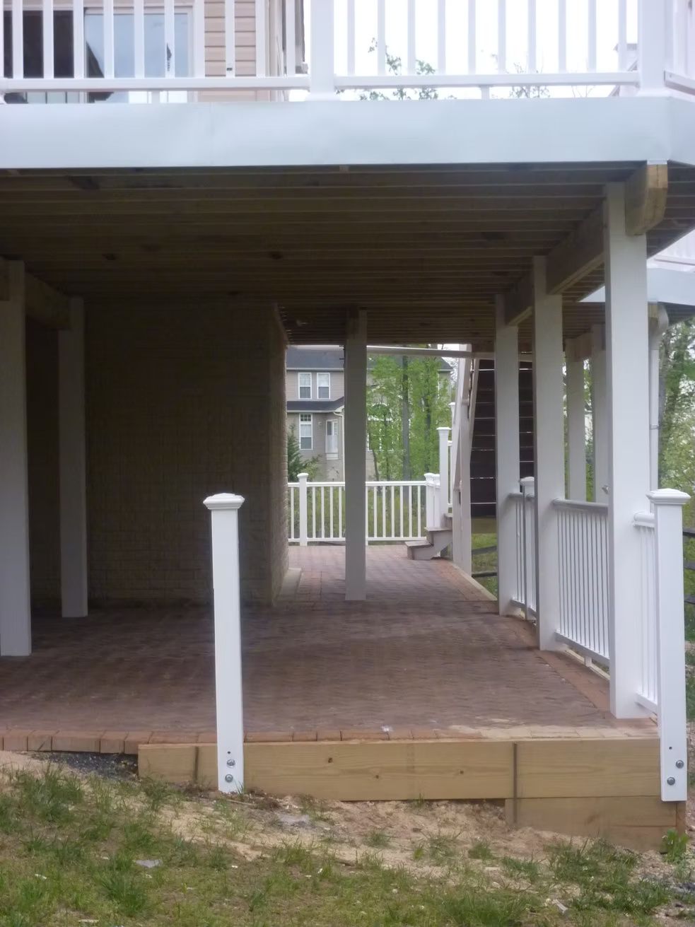 Covered wooden deck with white railings and posts, leading to a walkway between buildings