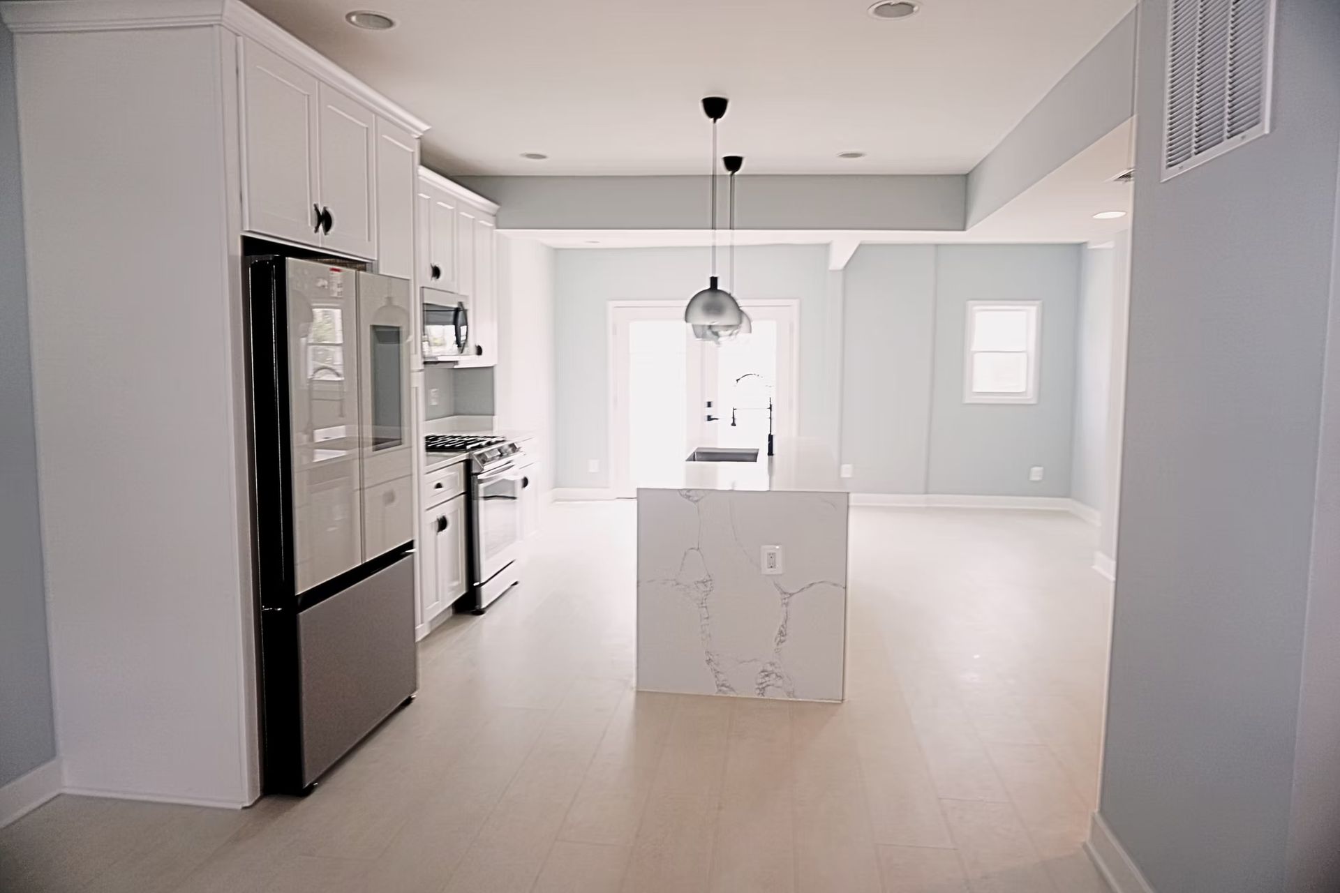 Bright modern kitchen with white cabinets, stainless fridge, island, and pendant light