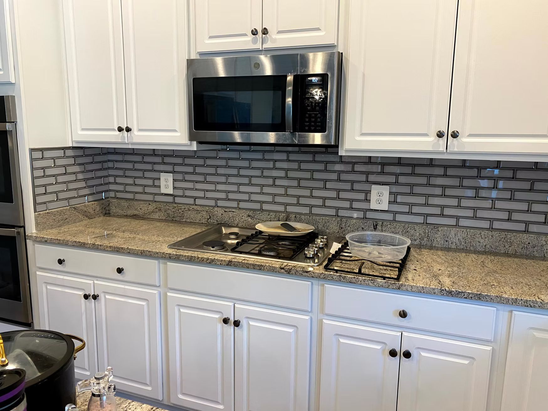 Modern kitchen with white cabinets, granite countertop, stainless microwave, and gray brick backsplash