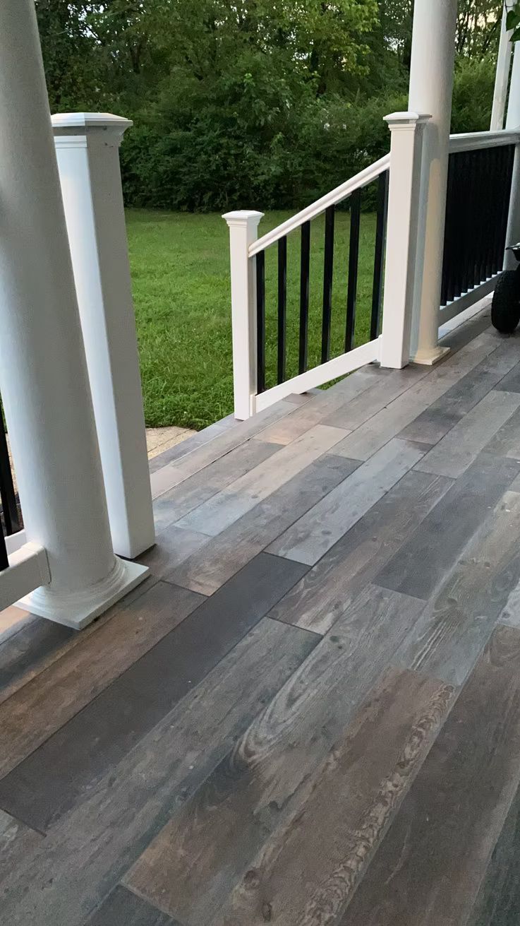 Porch with gray wood flooring, white railing, and a view of the green yard beyond.