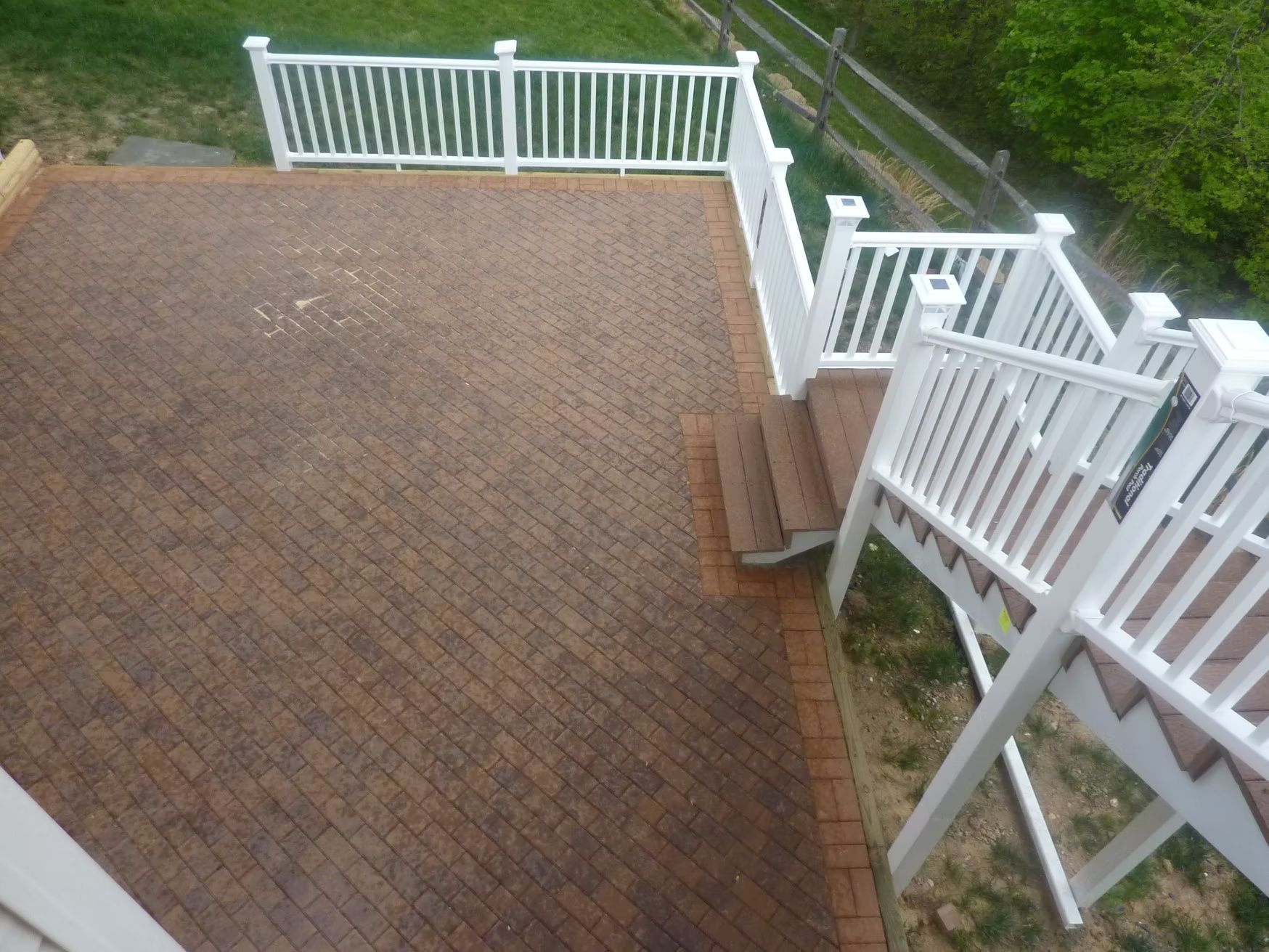 Brick patio with white railing and steps overlooking a green yard