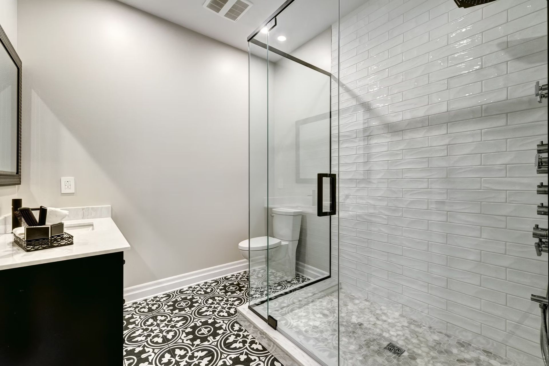 Modern bathroom with glass shower, black-and-white patterned floor, and white vanity counter