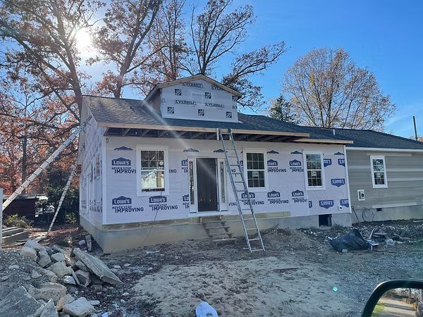 House under construction with white wrap, ladder at the front, and rubble in the yard.