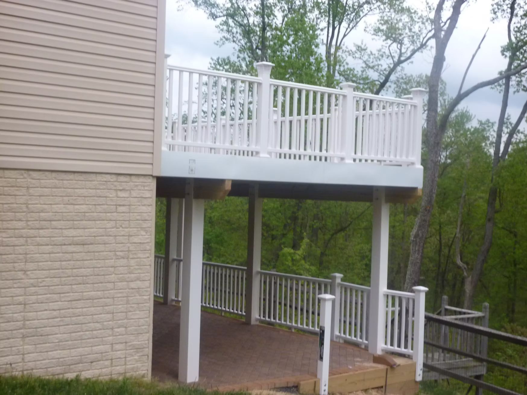 White elevated deck and staircase attached to a beige house beside a wooded backyard
