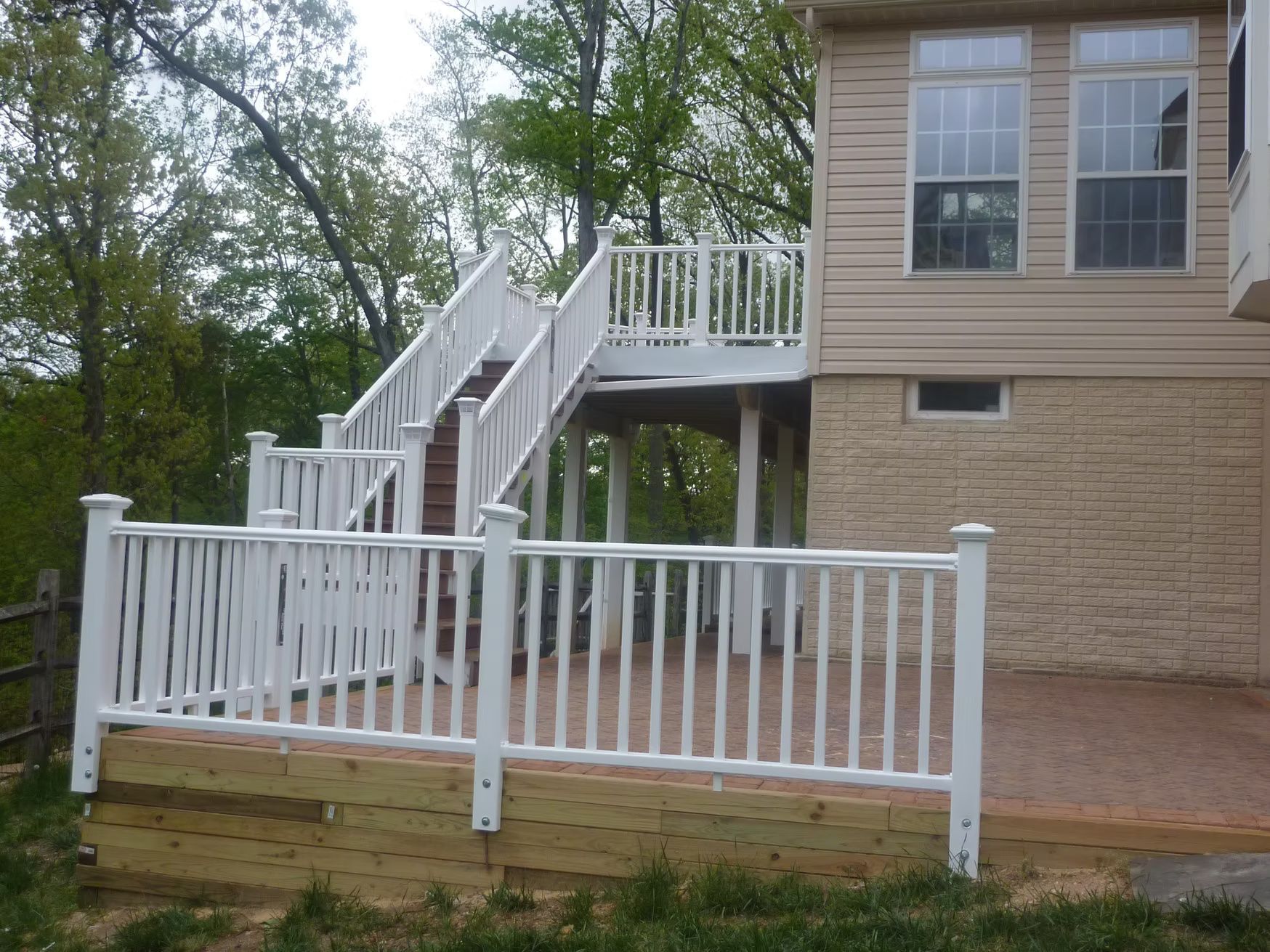 White wooden deck stairs and railings beside a tan house with a small fenced patio.