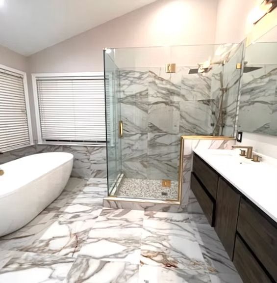 Luxurious marble bathroom with freestanding tub, glass shower, and dark vanity under a window