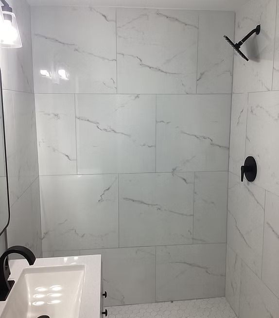 Modern white-tiled shower with black fixtures and a small sink in the foreground