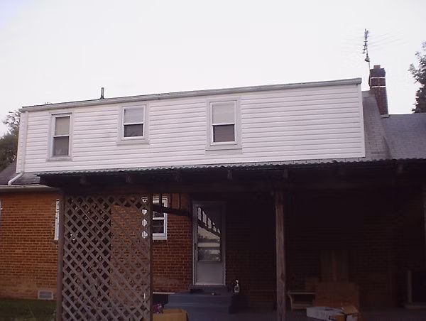 Two-story house with white upper siding, brick lower level, and a covered carport in front.