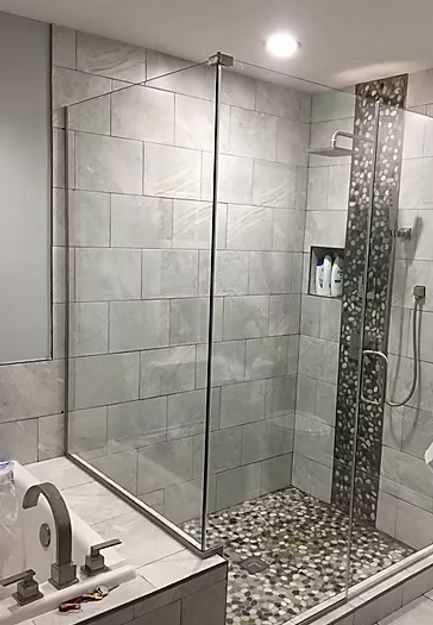 Modern bathroom shower with gray tile, glass enclosure, and pebble shower floor