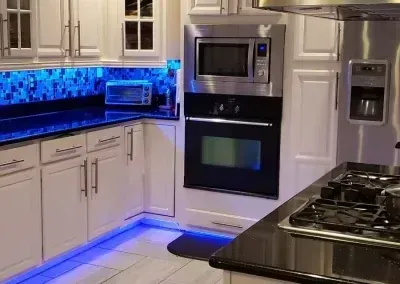 Modern white kitchen with blue under-cabinet lighting, stainless appliances, and a gas cooktop