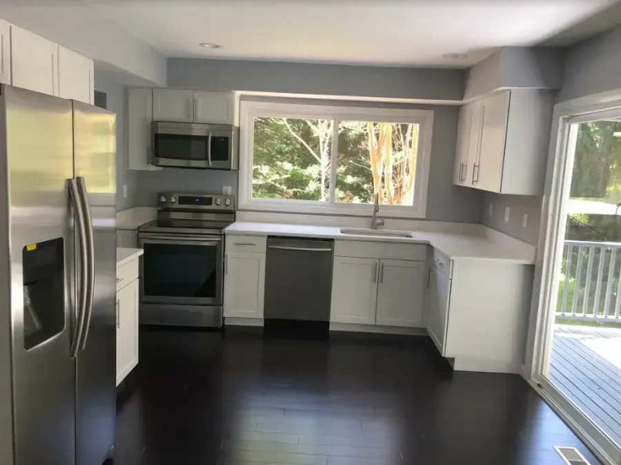 Bright modern kitchen with stainless appliances, gray cabinets, dark floor, and large windows.