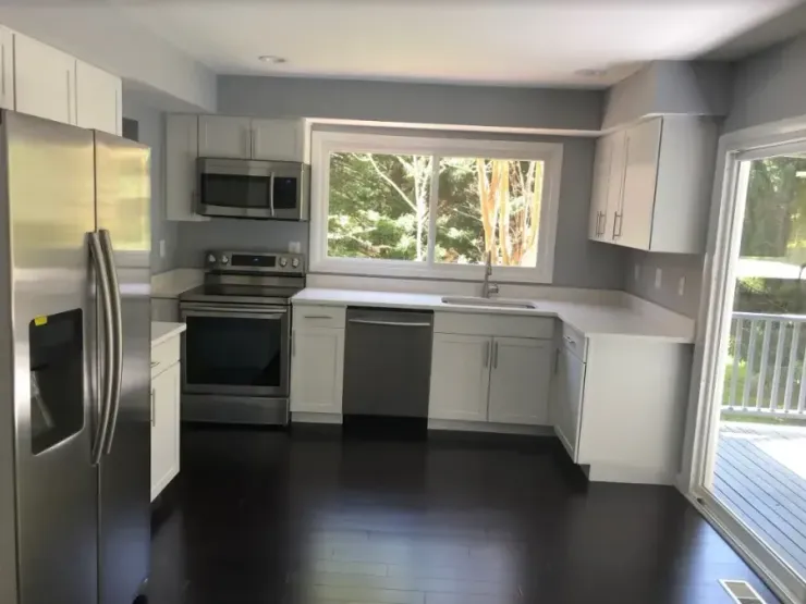 Bright kitchen with stainless steel appliances, white cabinets, dark floors, and a large window.