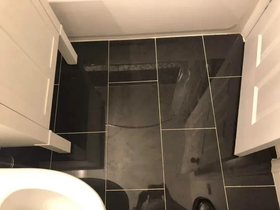 Black tiled bathroom floor with a toilet and white cabinets on both sides.