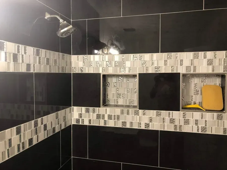 Tiled shower with black walls, gray mosaic border, and built-in shelves holding a yellow item.