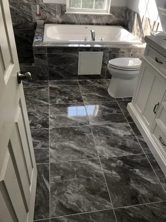 Modern bathroom with dark marble tile floor, white vanity, bathtub, and toilet.