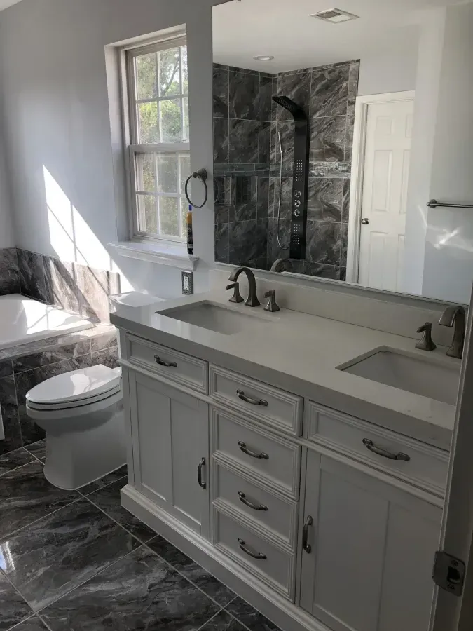 Modern bathroom with gray vanity, double sinks, large mirror, and dark marble tile shower