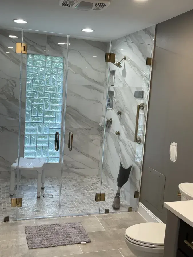 Modern bathroom with glass shower, gray marble walls, white vanity, and toilet