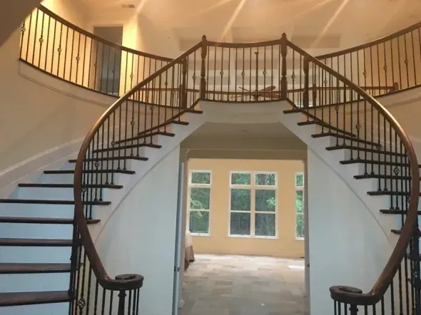 Curved double staircase with black railings in a foyer, facing a bright windowed wall.