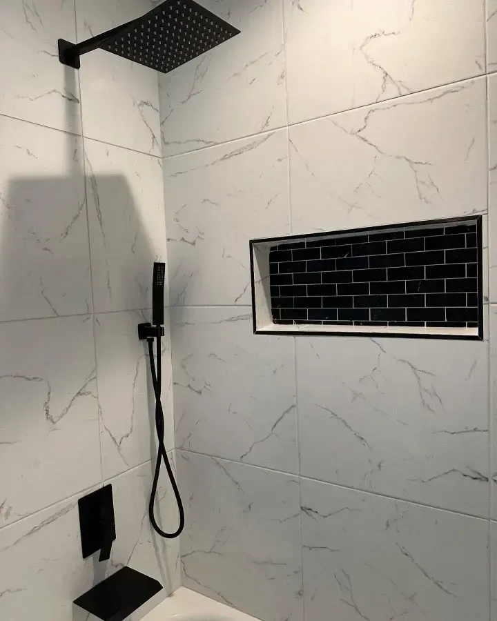 Modern shower with black rainfall head, handheld sprayer, marble-pattern tile, and black subway-tile niche