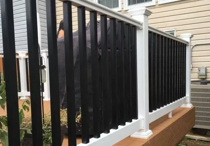 Black railing on a beige house porch with white posts and wood steps leading down to the yard