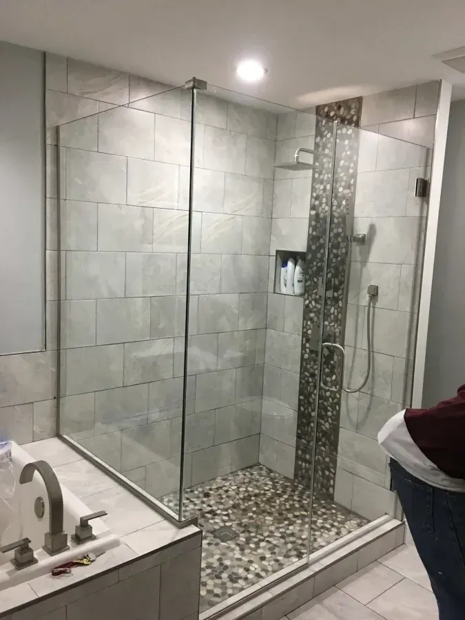 Modern tiled walk-in shower with glass enclosure, mosaic accent wall, and white sink in bathroom.