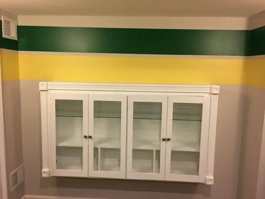 White cabinet mounted on a wall with green and yellow stripes near the ceiling.