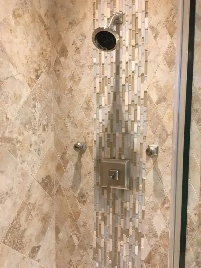 Walk-in shower with beige stone tile, mosaic accent strip, and chrome shower fixtures