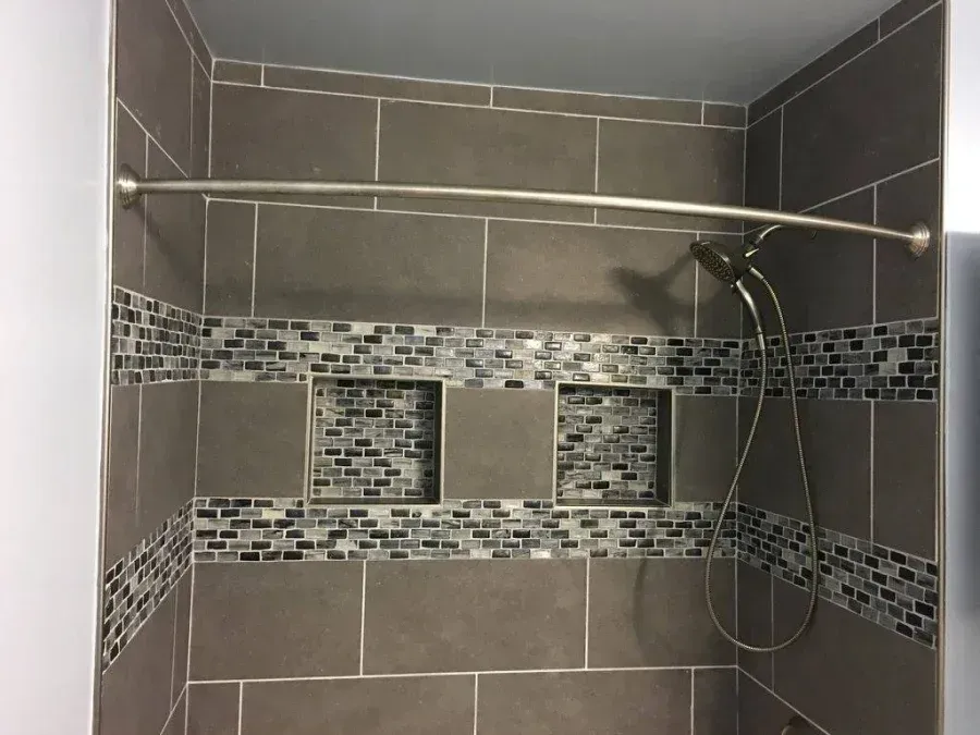 Tiled shower stall with gray walls, mosaic accent band, and handheld shower head