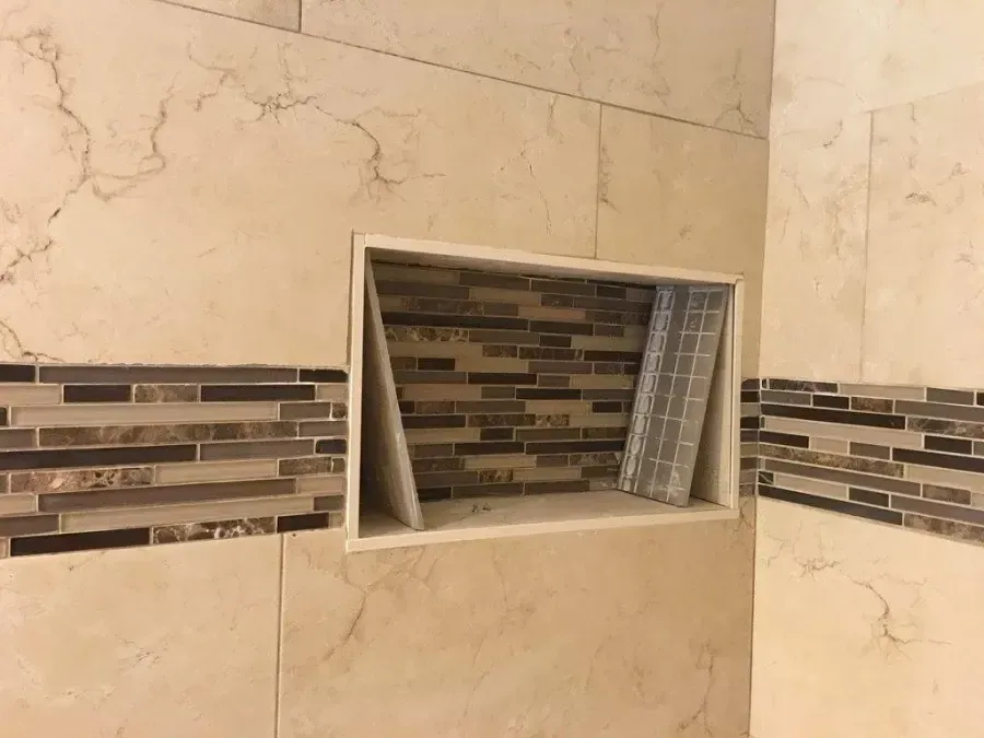Tiled bathroom wall with a rectangular recessed niche shelf and decorative mosaic accent strip