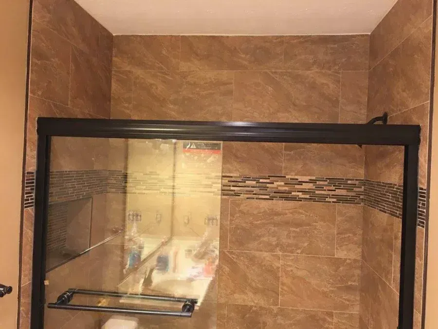 Empty glass shower enclosure with black frame in a beige tiled bathroom