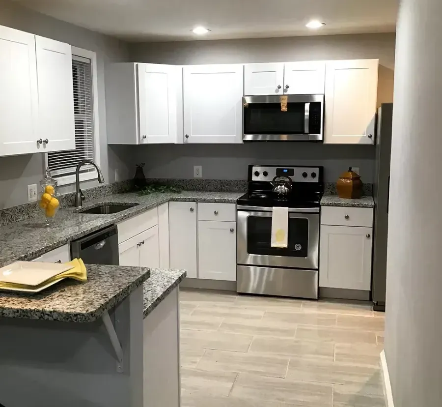 Modern kitchen with white cabinets, stainless steel appliances, granite counters, and light wood flooring