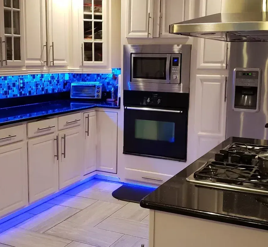 Modern white kitchen with blue under-cabinet lighting, stainless appliances, and black countertops