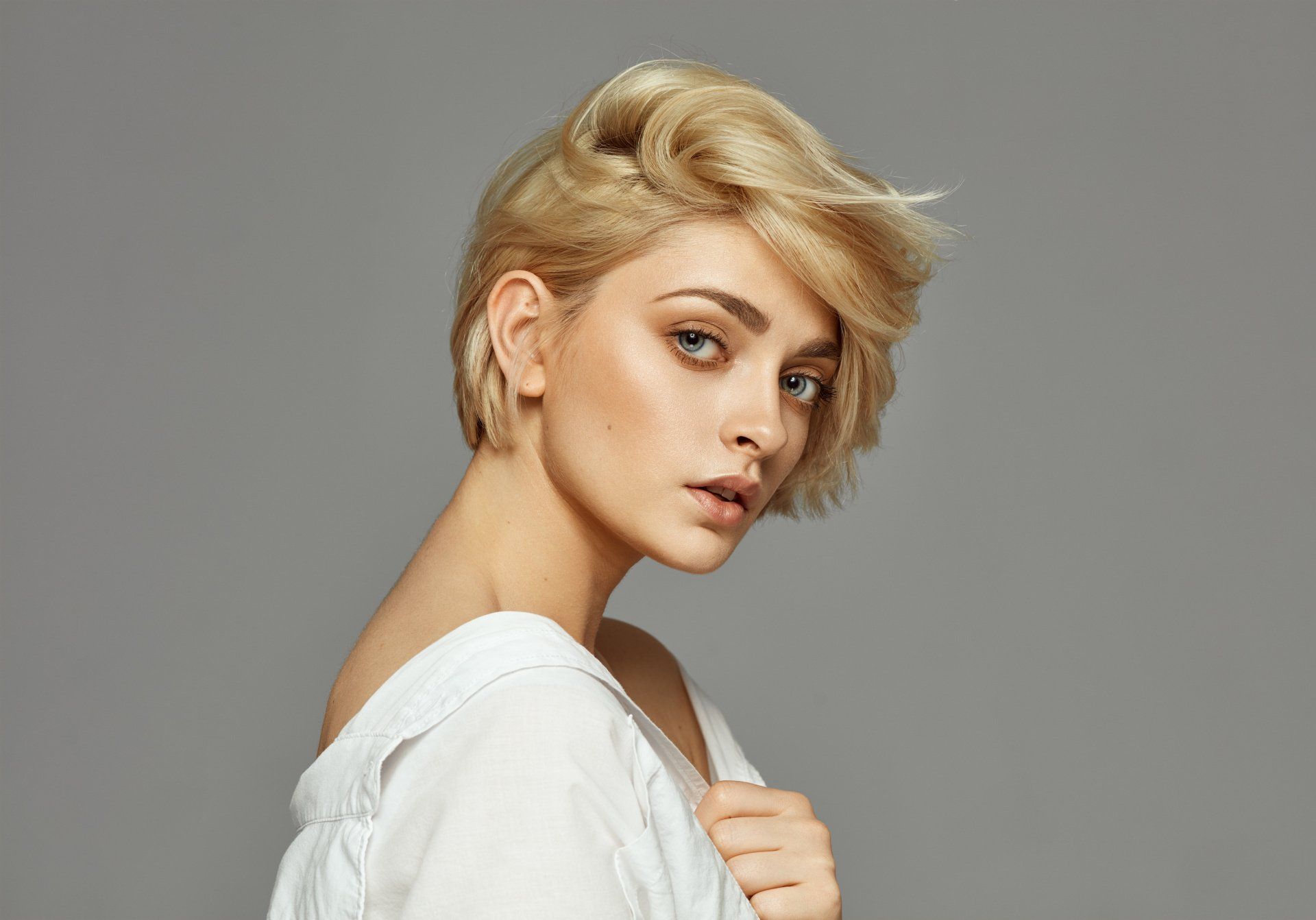 Eine Frau mit kurzen blonden Haaren trägt ein weißes Hemd und schaut in die Kamera.