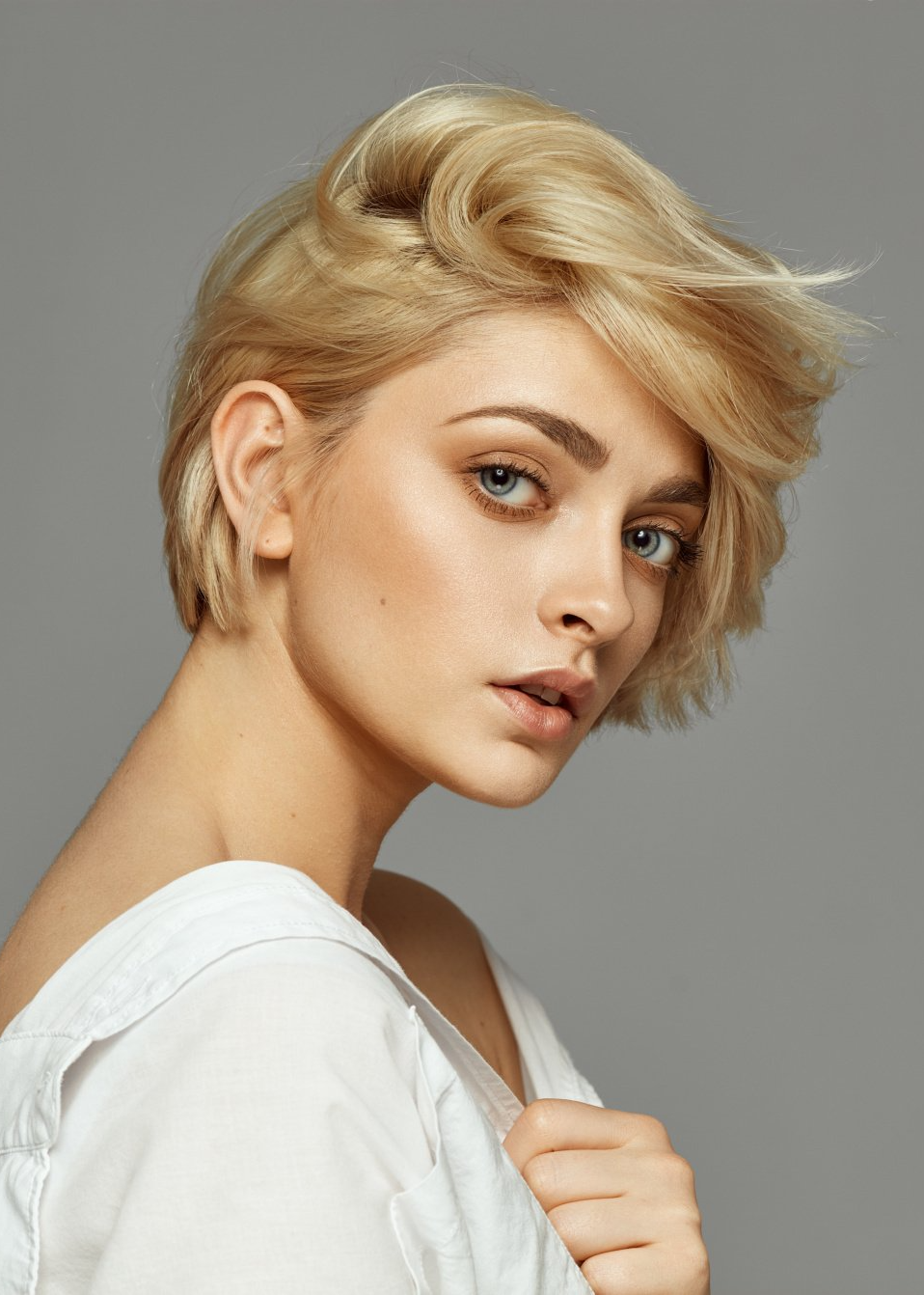 Eine Frau mit kurzen blonden Haaren trägt ein weißes Hemd und schaut in die Kamera.