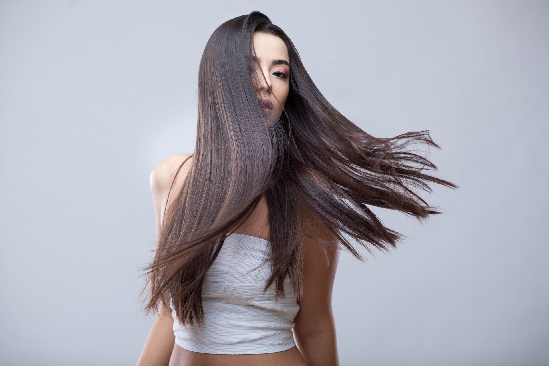 Eine Frau mit langen Haaren trägt ein weißes Oberteil und ihre Haare wehen im Wind.