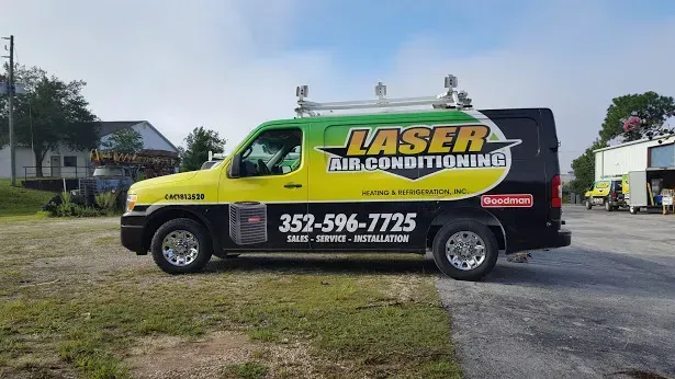Black, yellow, and green Laser Air Conditioning van parked on grass with phone number displayed.