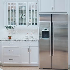 White kitchen cabinets with granite countertop and stainless steel refrigerator.