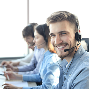 Group of people wearing headsets working at computers, smiling, in an office setting.