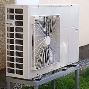 Outdoor white heat pump unit mounted on a metal stand, near a beige wall.
