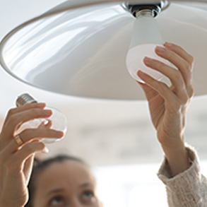 Person replacing a light bulb in a white lampshade. One hand holds the bulb, the other holds the old one.