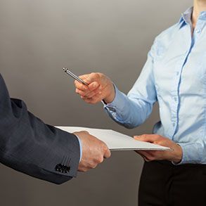 Person in blue shirt offers pen to another holding a document.