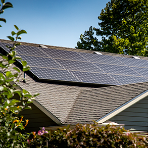 Solar panels installed on a residential rooftop. Blue sky and green trees in background.
