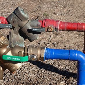 Two outdoor water shut-off valves with red and blue pipes. One valve has a green handle and is brass.